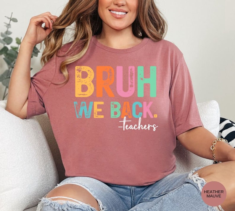 May include: A heather mauve t-shirt with the text "BRUH WE BACK. -teachers" in colorful letters. The letters are in a distressed font.