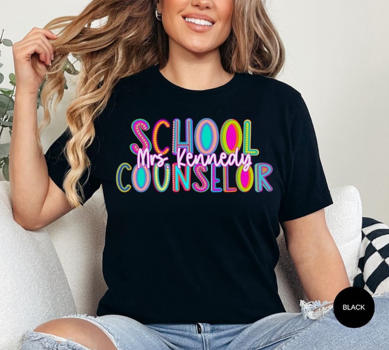 May include: Black t-shirt with the text "SCHOOL COUNSELOR" in colorful letters with a white outline. The text "Mrs. Kennedy" is written in white letters below the word "SCHOOL".