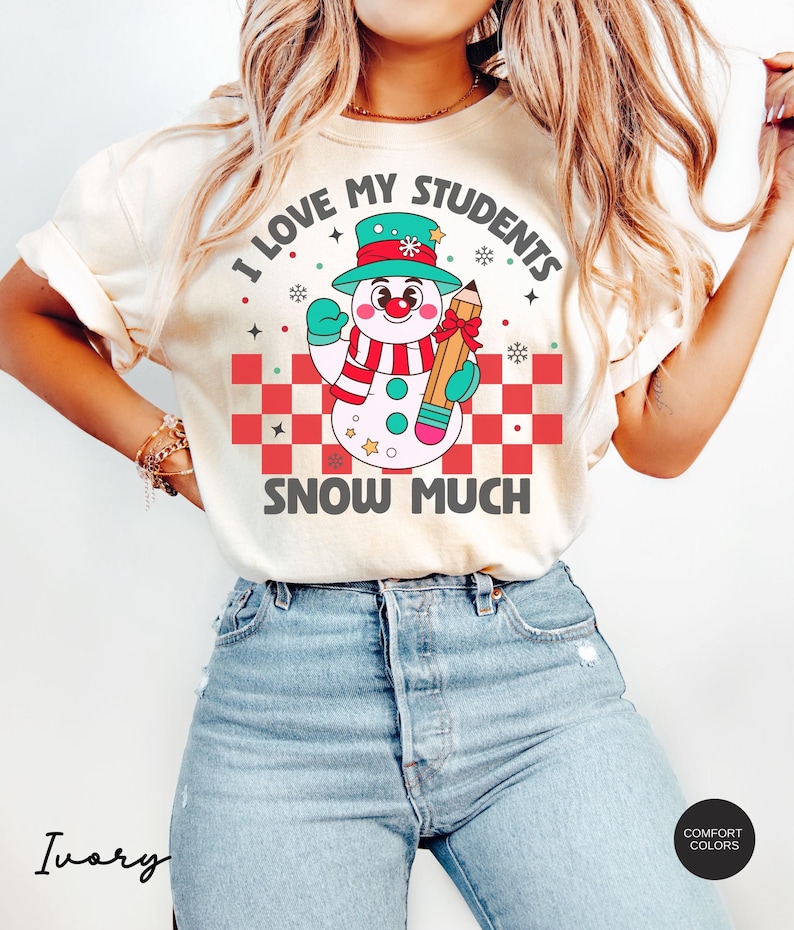 May include: A white t-shirt with a snowman graphic and the text "I love my students snow much". The snowman is wearing a green hat, a blue scarf, and holding a pencil. The background is a red and white checkered pattern.