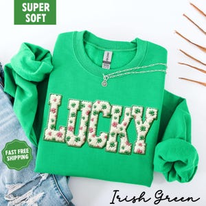 Pu&ograve; includere: Una felpa verde con la scritta "LUCKY" ricamata sul davanti con un motivo floreale. La felpa ha un girocollo e maniche lunghe. &Egrave; visibile una collana d'argento con un ciondolo. Le parole "Irish Green" sono scritte in corsivo.