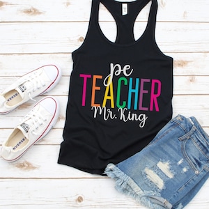 K&ouml;nnte beinhalten: Schwarzes Tanktop mit dem Text "pe teacher Mr. King" in Regenbogenfarben. Der Text ist in einer handschriftlichen Schriftart.