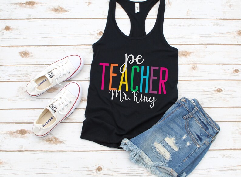 K&ouml;nnte beinhalten: Schwarzes Tanktop mit dem Text "pe teacher Mr. King" in Regenbogenfarben. Der Text ist in einer handschriftlichen Schriftart.