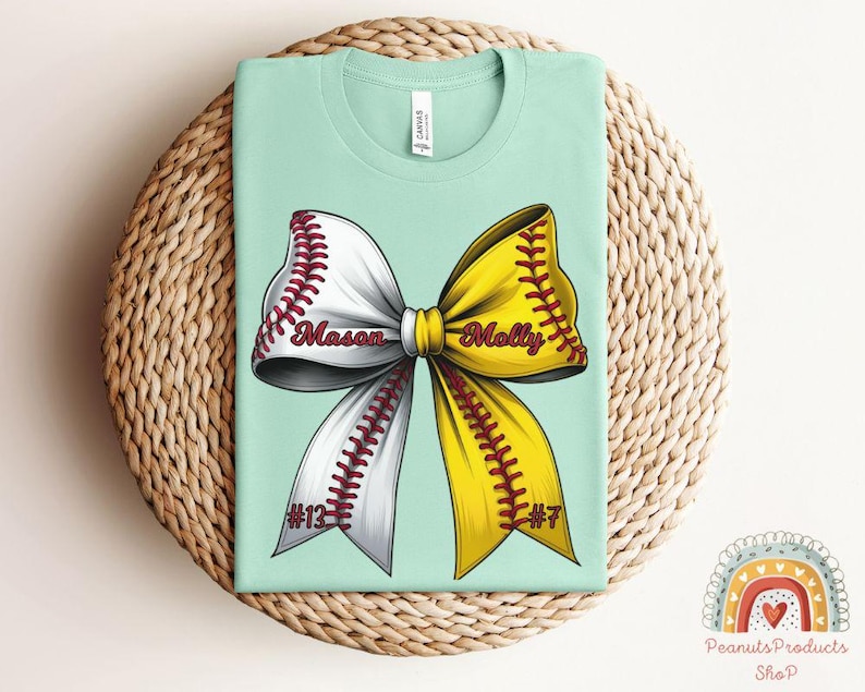 May include: A light blue t-shirt with a softball bow design. The bow is yellow and white with red stitching. The words "Mason" and "Molly" are written on the bow. The numbers "#13" and "#7" are on the bottom of the bow.