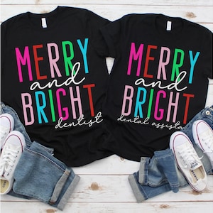 May include: Two black t-shirts with the text "Merry and Bright" in colorful letters. One shirt says "dentist" and the other says "dental assistant".