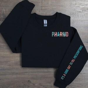 May include: Black sweatshirt with the text "PHARMD" in colorful letters on the front and the text "IT'S A GOOD DAY TO FILL PRESCRIPTIONS" on the sleeve.