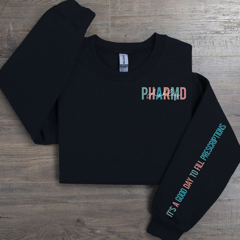 May include: Black sweatshirt with the text "PHARMD" in colorful letters on the front and the text "IT'S A GOOD DAY TO FILL PRESCRIPTIONS" on the sleeve.