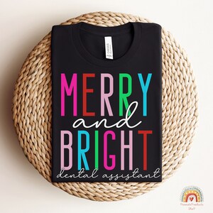 May include: Black t-shirt with the text "Merry and Bright dental assistant" in colorful letters.
