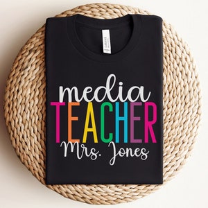 K&ouml;nnte beinhalten: Schwarzes T-Shirt mit dem Text "media teacher Mrs. Jones" in Regenbogenfarben.