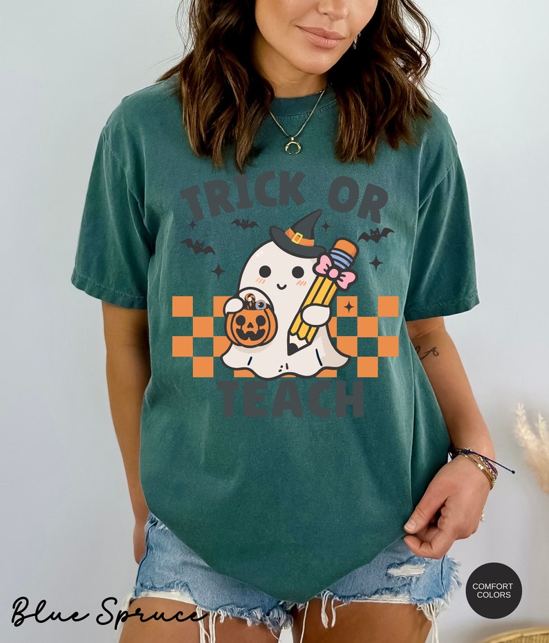 K&ouml;nnte beinhalten: Ein blaugr&uuml;nes T-Shirt mit einem Motiv eines Geistes, der einen Hexenhut tr&auml;gt und einen Bleistift und einen K&uuml;rbis h&auml;lt. Der Text "Trick or Teach" ist auf das Shirt gedruckt.