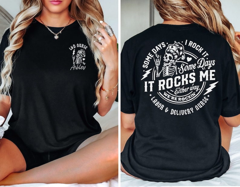 K&ouml;nnte beinhalten: Schwarzes T-Shirt mit einem wei&szlig;en Grafikdruck eines Skeletts, das einen Blitz und ein Herz h&auml;lt. Der Text lautet "Some days I rock it, some days it rocks me - Either way, we're rockin' - Labor & Delivery Nurse".