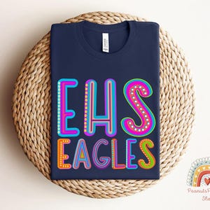 Puede incluir: Camiseta azul marino con un gr&aacute;fico colorido que dice "EHS Eagles".
