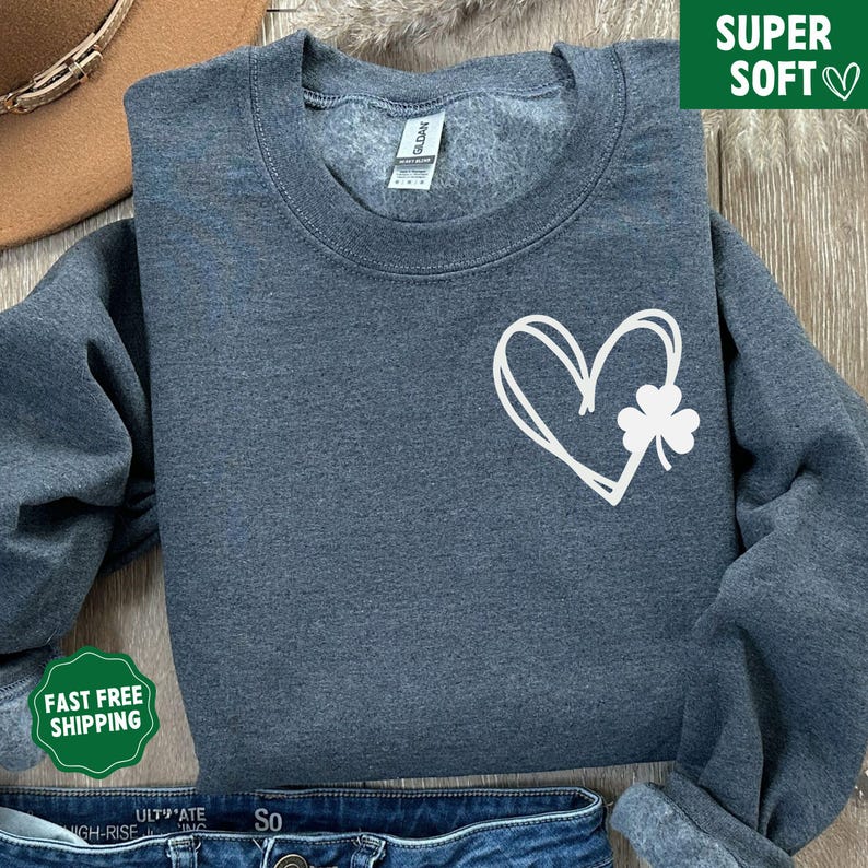 May include: A dark grey sweatshirt featuring a white heart and shamrock design. The sweatshirt is made from a soft, comfortable material.