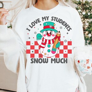 May include: White t-shirt with a snowman holding a pencil and the text "I love my students snow much".