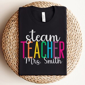 K&ouml;nnte beinhalten: Schwarzes T-Shirt mit dem Text "steam teacher" in Regenbogenfarben und "Mrs. Smith" in Wei&szlig; darunter.