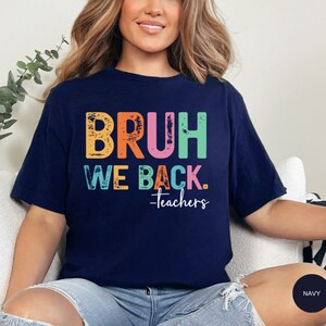 May include: A navy blue t-shirt with the text "BRUH WE BACK. -Teachers" in rainbow colors. The text has a distressed, vintage look.