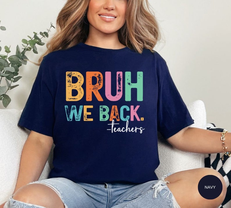 May include: A navy blue t-shirt with the text "BRUH WE BACK. -Teachers" in rainbow colors. The text has a distressed, vintage look.