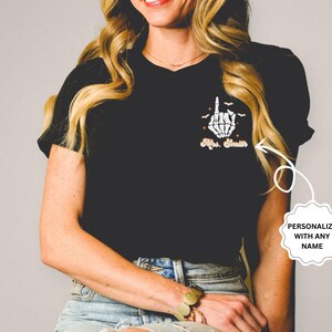 Puede incluir: Camiseta negra con una mano de esqueleto haciendo el dedo medio y el texto "Mrs. Smith".