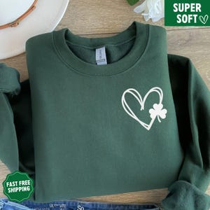 May include: A dark green sweatshirt with a white outline of a heart and a shamrock inside the heart.