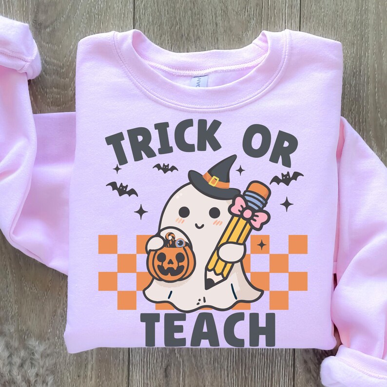 May include: Pink sweatshirt with a ghost holding a pencil and a pumpkin. The text "Trick or Teach" is printed on the sweatshirt.