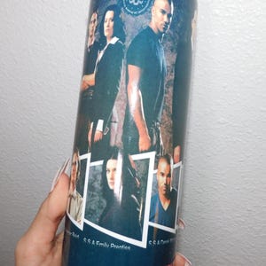 Könnte beinhalten: Ein Edelstahlbecher mit einer Collage von Bildern von Schauspielern der Fernsehserie Criminal Minds. Der Becher hat einen blauen Hintergrund mit dem Logo der Show in Rot. Der Becher ist zylindrisch und hat einen silbernen Deckel.