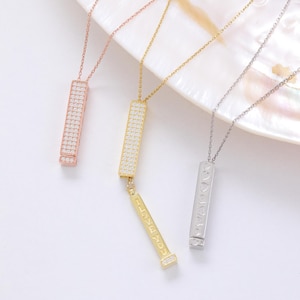 Puede incluir: Tres collares con colgantes en oro rosa, oro y plata. Los colgantes de oro rosa y oro son rectangulares e incrustados con pequeñas piedras transparentes. El colgante de oro tiene una pieza más pequeña colgante con las palabras "LOVE MADE" grabadas. El colgante de plata tiene formas de corazón y estrella.