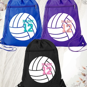 May include: Three drawstring backpacks in blue, purple, and black. Each bag features a white volleyball design with the word "NAME" and the number "12" in a contrasting color. The bags have a zippered front pocket and a drawstring closure.
