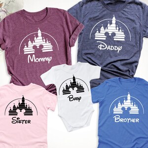 May include: A collection of family t-shirts and a baby bodysuit in shades like burgundy, navy, pink, white, and blue. Each garment displays a white castle graphic with Mickey Mouse ears and a family role: Mommy, Daddy, Baby, Sister, and Brother.