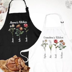 May include: Two aprons, one black and one white, each with floral designs and text. The black apron says "Mama's Kitchen" with names below the flowers. The white apron says "Grandma's Kitchen" with names below the flowers.