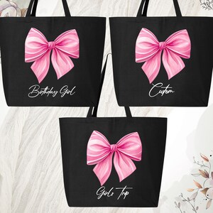 May include: Black tote bags with large pink bow designs. One bag reads "Birthday Girl", another "Custom", and the third "Girls Trip". The bags have long black handles and are likely made of canvas or a similar material.