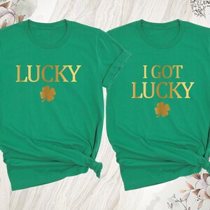 K&ouml;nnte beinhalten: Zwei gr&uuml;ne T-Shirts mit goldenem Text und einem goldenen Kleeblatt. Ein Shirt sagt "LUCKY" und das andere sagt "I GOT LUCKY". Die Shirts sind wahrscheinlich f&uuml;r St. Patrick's Day.