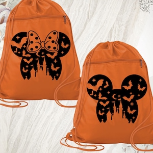 May include: Two orange drawstring bags with black Halloween-themed designs. One bag features a bow with polka dots, bats, and a castle. The other bag has a Mickey Mouse head shape with bats, stars, and a castle. Both bags have a zipper pocket.