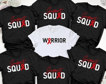 May include: Six black t-shirts with white text and a red ribbon design. The text on the shirts says "Support Squad" and one shirt says "Warrior".