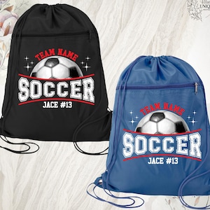 May include: Two drawstring soccer bags, one black and one blue. Each bag features a soccer ball graphic with the word "SOCCER" in white, and the text "TEAM NAME" and "JACE #13". The bags have a zippered pocket.