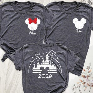 May include: Three dark heather gray t-shirts. Two shirts feature a white mouse-ear silhouette on the chest; one has a red bow and the text "Mom," the other has the text "Dad." The third shirt displays a white castle graphic with "2026" below.
