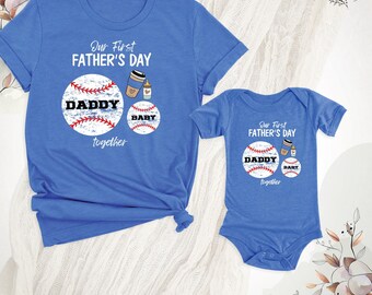 May include: A blue short-sleeved t-shirt and a matching blue baby bodysuit. Both feature a graphic with two baseballs labeled DADDY and BABY, a coffee cup, a baby bottle, and the text Our First FATHER'S DAY together in white lettering.