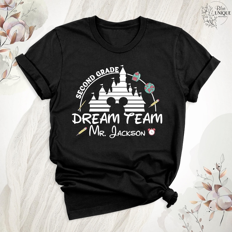 May include: Black t-shirt with a white graphic featuring a castle, Mickey Mouse ears, and the words "SECOND GRADE DREAM TEAM Mr. Jackson." Includes school-themed illustrations like pencils, a backpack, and a globe.