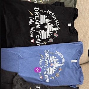 May include: Four t-shirts in olive green, black, blue, and charcoal gray. Each shirt features a white graphic with the words "DREAM TEAM" and "FOURTH GRADE" around a castle and Mickey Mouse silhouette. The teacher's name is also printed on each shirt.