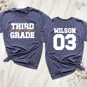以下が含まれることがあります： 紺色のTシャツ2枚。1枚には白とオレンジ色の文字で「THIRD dream team GRADE」と書かれています。もう1枚には白で「WILSON 03」と書かれています。どちらも裾が結ばれています。学校やスポーツに最適です。