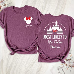 K&ouml;nnte beinhalten: Zwei weinrote T-Shirts mit wei&szlig;en Grafiken. Eines zeigt einen Minnie-Mouse-Kopf mit roter Schleife und dem Wort "Oma". Das andere hat ein Schlossdesign mit dem Text "MOST LIKELY TO Be Taking Photos."