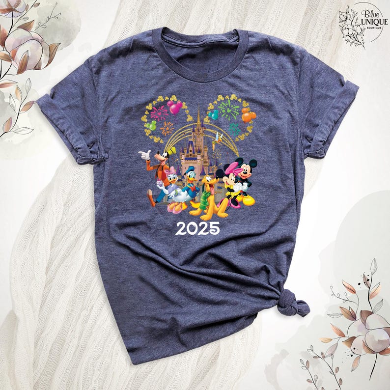 Puede incluir: Una camiseta azul oscuro con un gr&aacute;fico de Mickey Mouse, Minnie Mouse, Donald Duck, Goofy y Pluto frente al Castillo de Cenicienta con fuegos artificiales. El texto "2025" est&aacute; impreso debajo de los personajes.