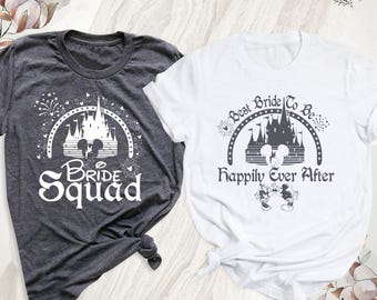 Könnte beinhalten: Ein dunkelgraues T-Shirt mit einer weißen Schlossgrafik und dem Text Bride Squad sowie ein weißes T-Shirt mit einer dunkelgrauen Schlossgrafik, dem Text Best Bride To Be Happily Ever After und zwei Mausfiguren.