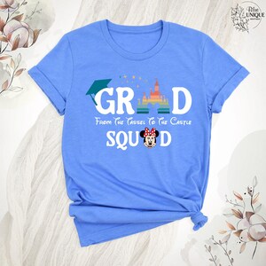 Puede incluir: Camiseta azul claro con un gr&aacute;fico de un gorro de graduaci&oacute;n, la palabra "GRAD", un castillo arco&iacute;ris y el texto "From the tassel to the castle SQUAD". Una imagen de dibujos animados de Minnie Mouse est&aacute; en el medio del texto "SQUAD".