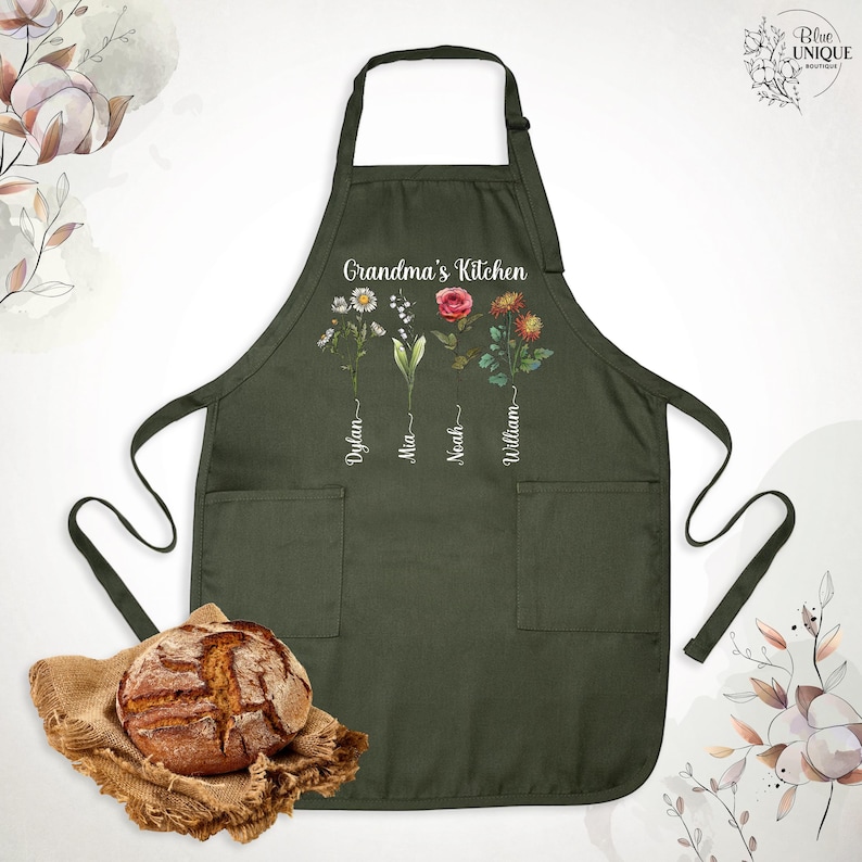 May include: An olive green apron with the text "Grandma's Kitchen" and floral designs. The apron features pockets and the names Dylan, Mia, Noah, and William. A loaf of bread rests on a burlap cloth in the foreground.