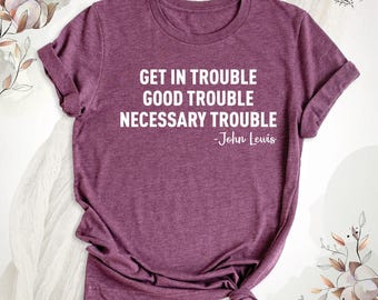 May include: A heathered maroon short-sleeve t-shirt featuring white text that reads: GET IN TROUBLE GOOD TROUBLE NECESSARY TROUBLE -John Lewis. The shirt has a crew neckline and a casual fit with rolled sleeves.