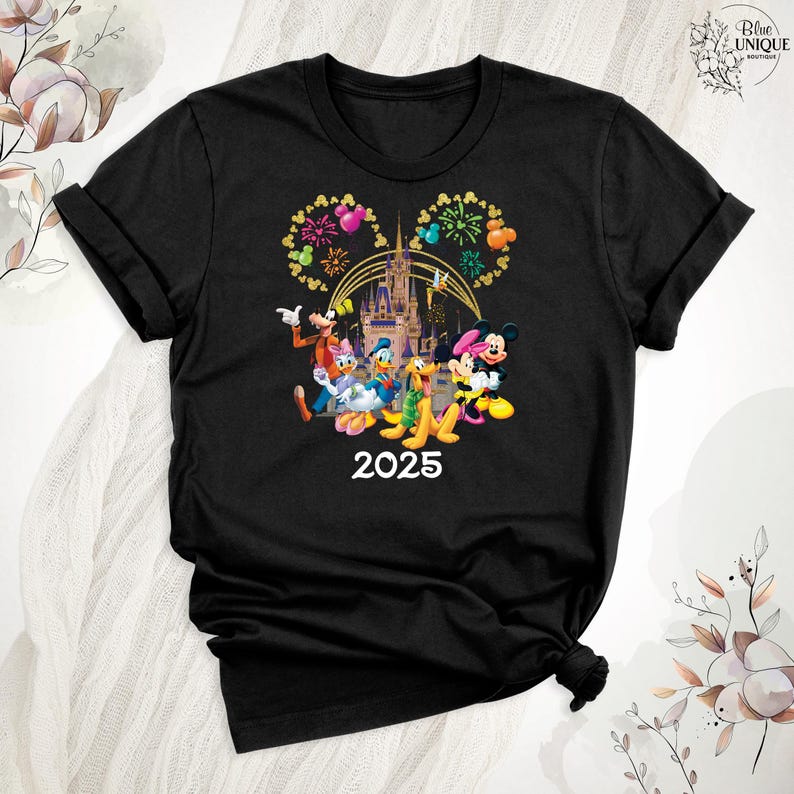 Puede incluir: Camiseta negra con un gr&aacute;fico de Mickey Mouse y sus amigos frente al Castillo de Cenicienta con fuegos artificiales. El texto "2025" est&aacute; debajo del gr&aacute;fico.