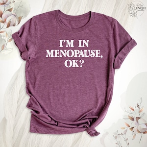 May include: A maroon t-shirt with the text "I'm in Menopause, OK?" printed in white.