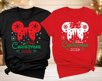 May include: A black t-shirt and a red t-shirt featuring a graphic of a Mickey Mouse silhouette containing a castle and snowflakes. The text reads Disney Christmas 2026. The red shirt includes a polka-dot bow on the Mickey ears silhouette.