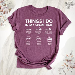 Op de afbeelding: Een maron T-shirt met de tekst "THINGS I DO IN MY SPARE TIME" en een lijst met autogerelateerde activiteiten, waaronder "DRIVE CARS", "RESEARCH CARS", "TAKE CARE OF MY CAR", "TALK ABOUT CARS", "THINK ABOUT CARS" en "DREAM ABOUT CARS".