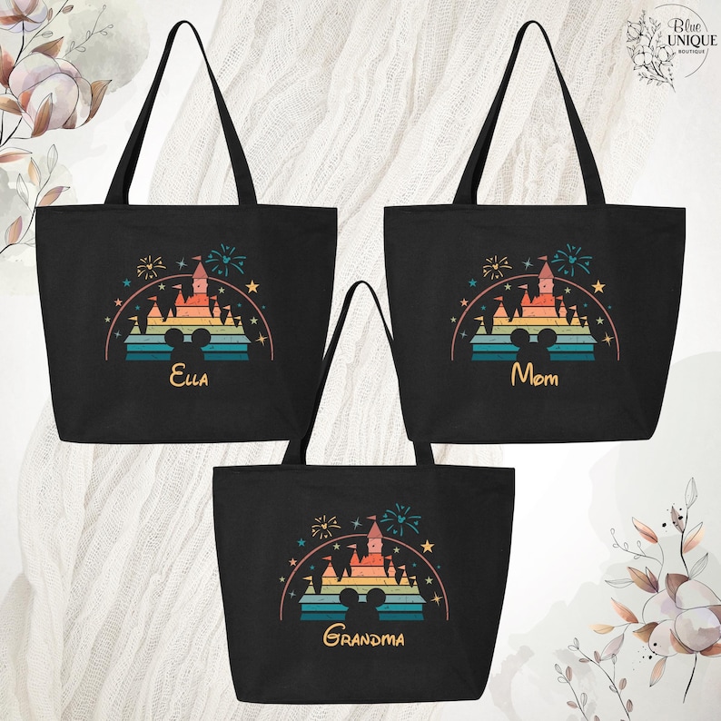 May include: Three black canvas tote bags with a retro rainbow design of a castle with fireworks and a Mickey Mouse silhouette. The bags are personalized with the names "Ella", "Mom", and "Grandma".