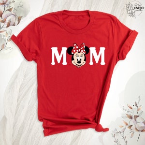 K&ouml;nnte beinhalten: Rotes T-Shirt mit einem wei&szlig;en "MOM"-Aufdruck, der eine Comic-Minnie Maus mit einer roten Schleife und wei&szlig;en Punkten zeigt.